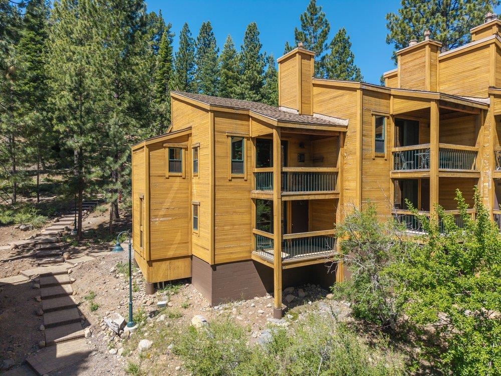 Wood-sided mountain residence with stacked balconies, pine trees, and a stepped path.