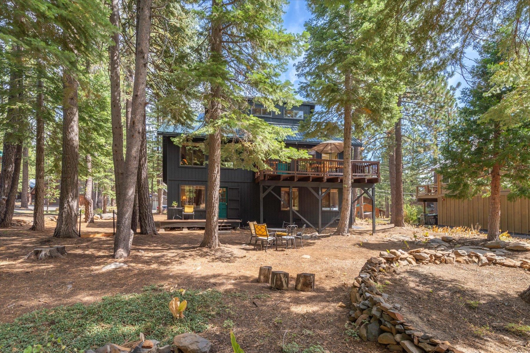 Dark two-story home among pines with an elevated deck and outdoor dining area.