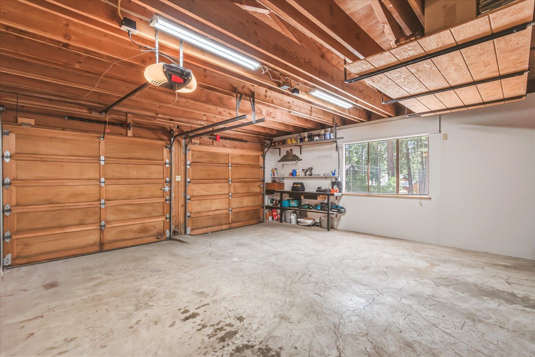 Two-car garage with wooden doors, exposed beams, overhead storage, and a tool-lined workbench.
