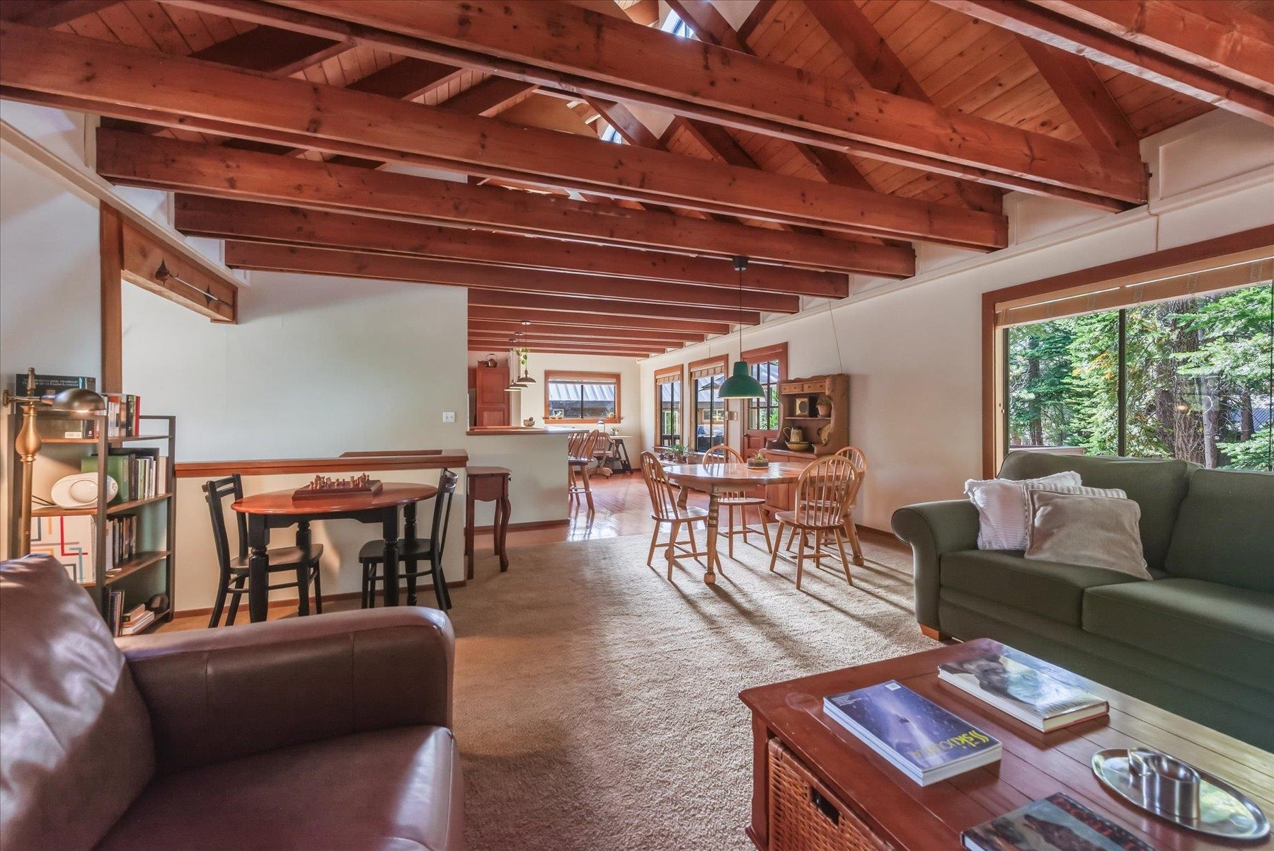 Open-plan living and dining room with exposed timber beams and large windows overlooking trees.