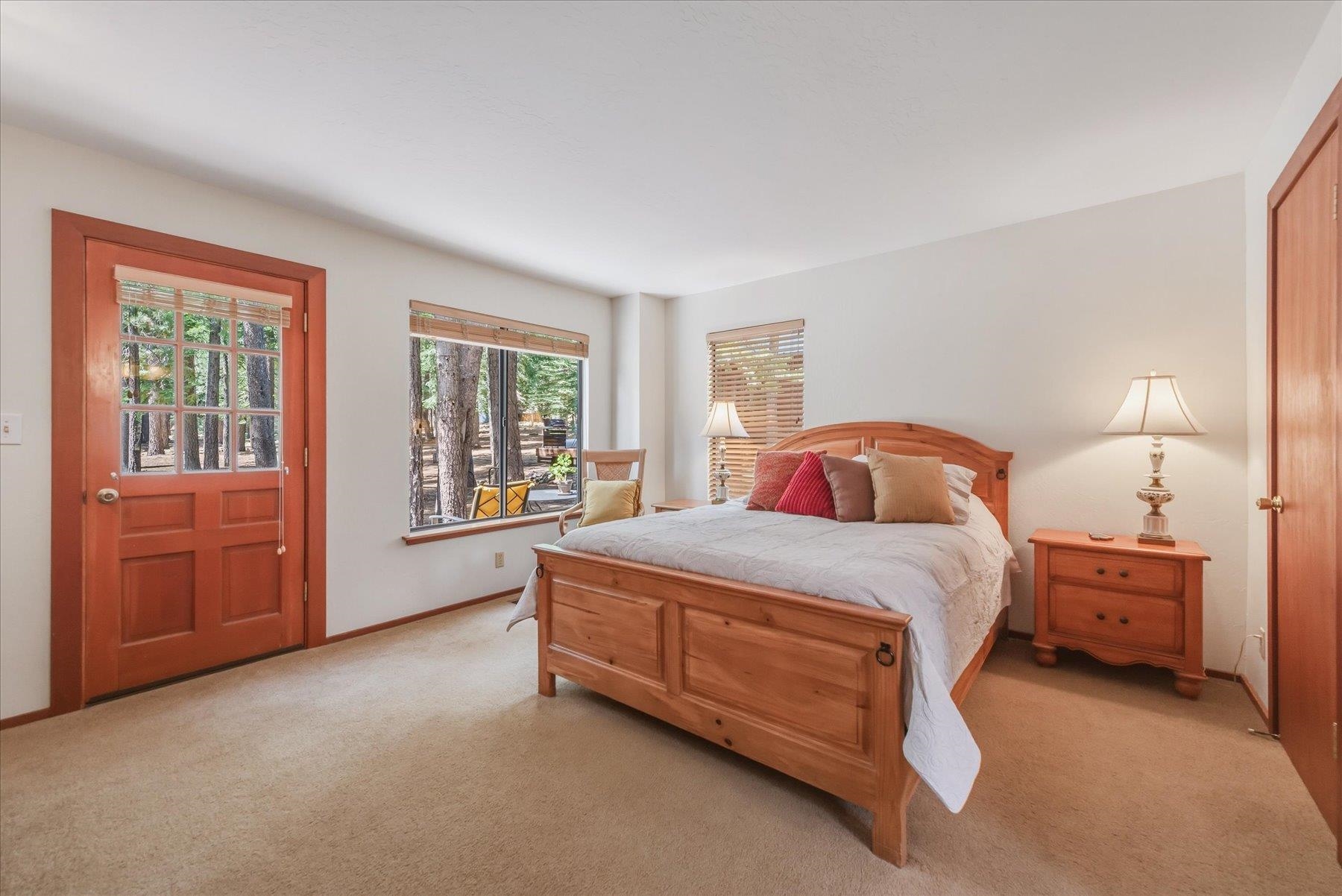 Furnished bedroom with a large wooden bed and views of trees through the door and window.