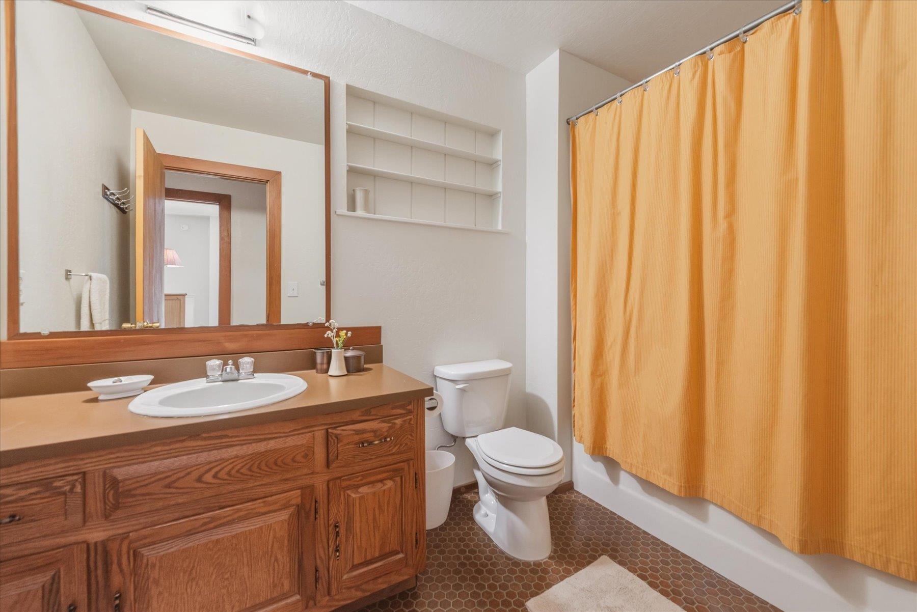 Bathroom with a wood vanity, toilet, and bathtub behind an orange shower curtain.
