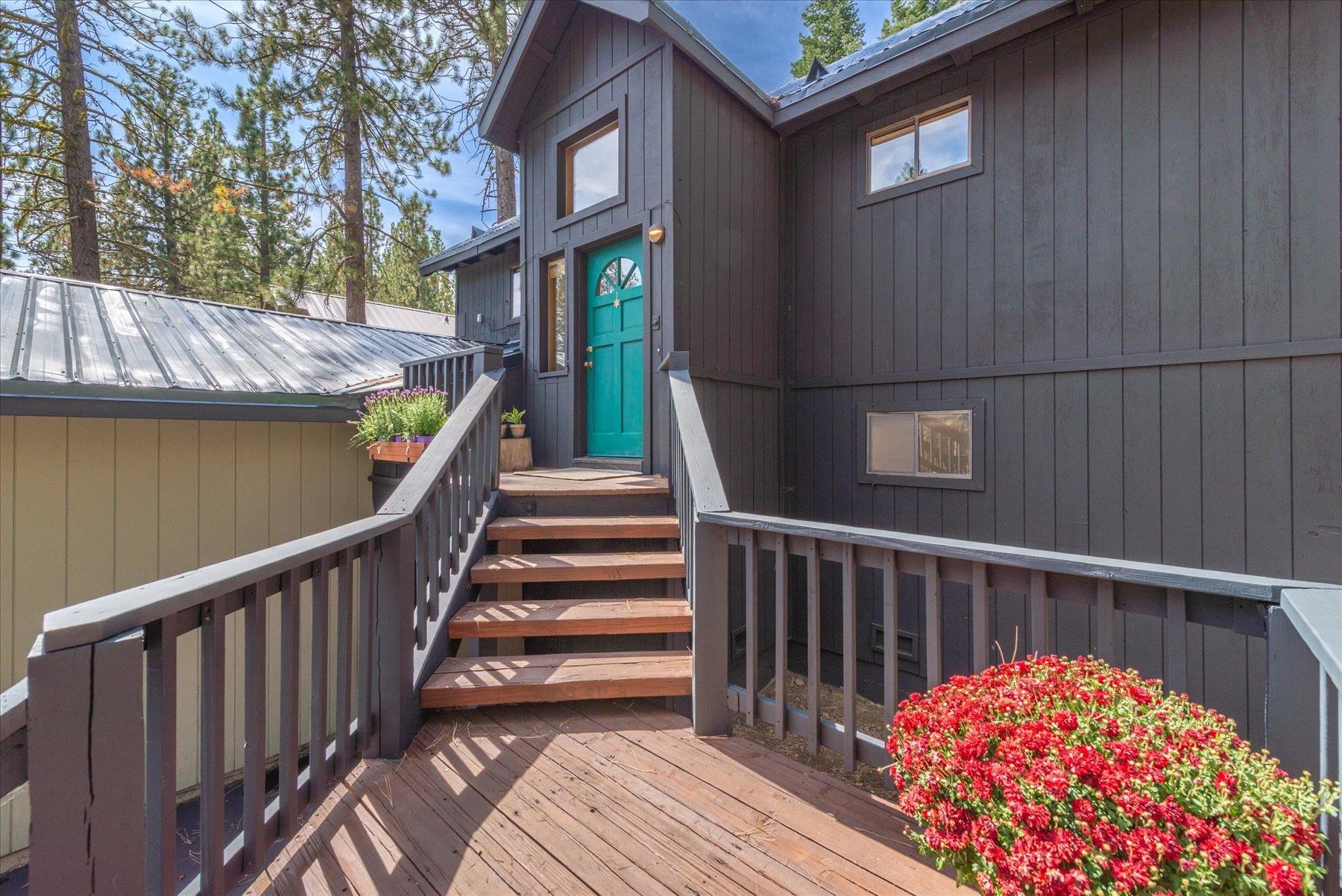 Dark-sided home entrance with a teal door, wooden stairs, and red flowers.