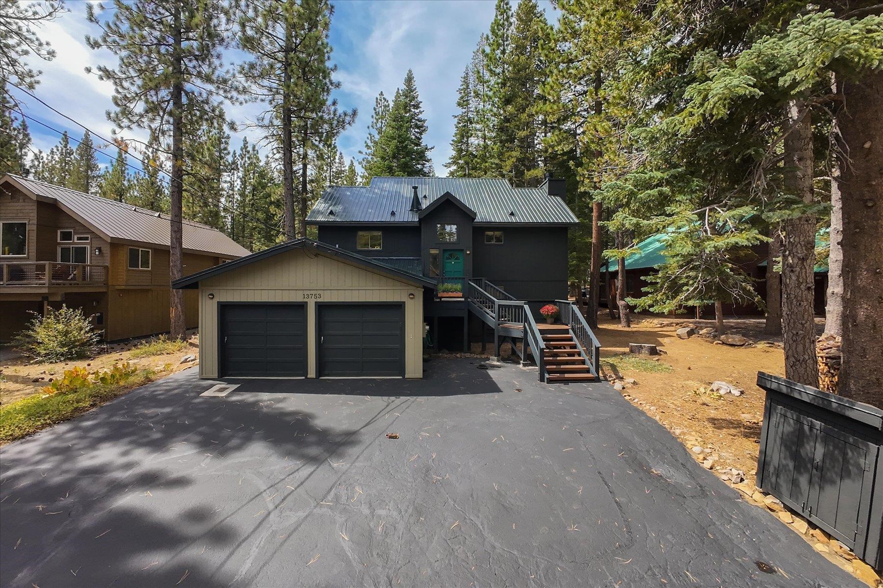 Dark Truckee home with a metal roof, teal entry door, double garage, and pine trees.