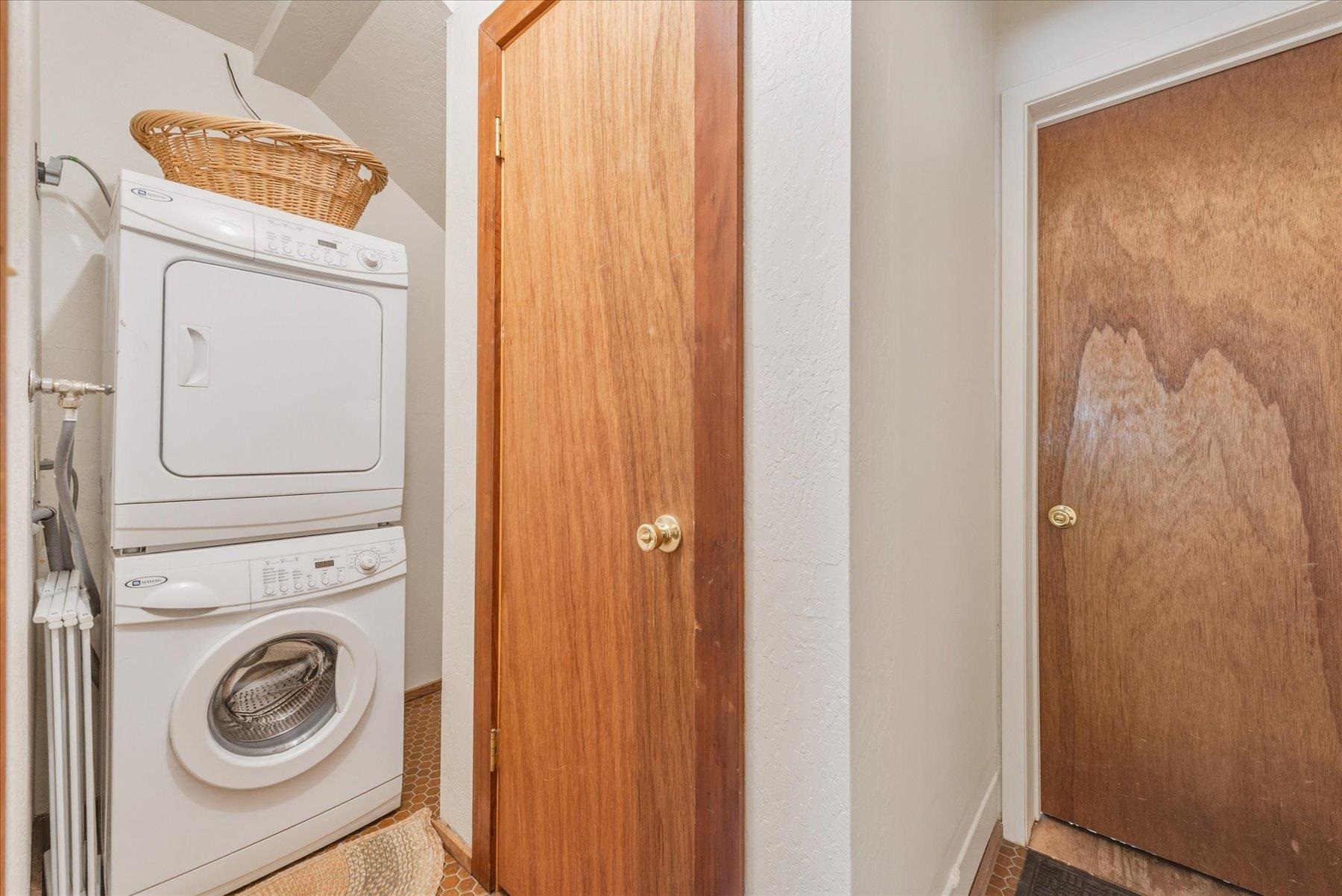 Laundry nook with stacked washer and dryer beside wooden doors.