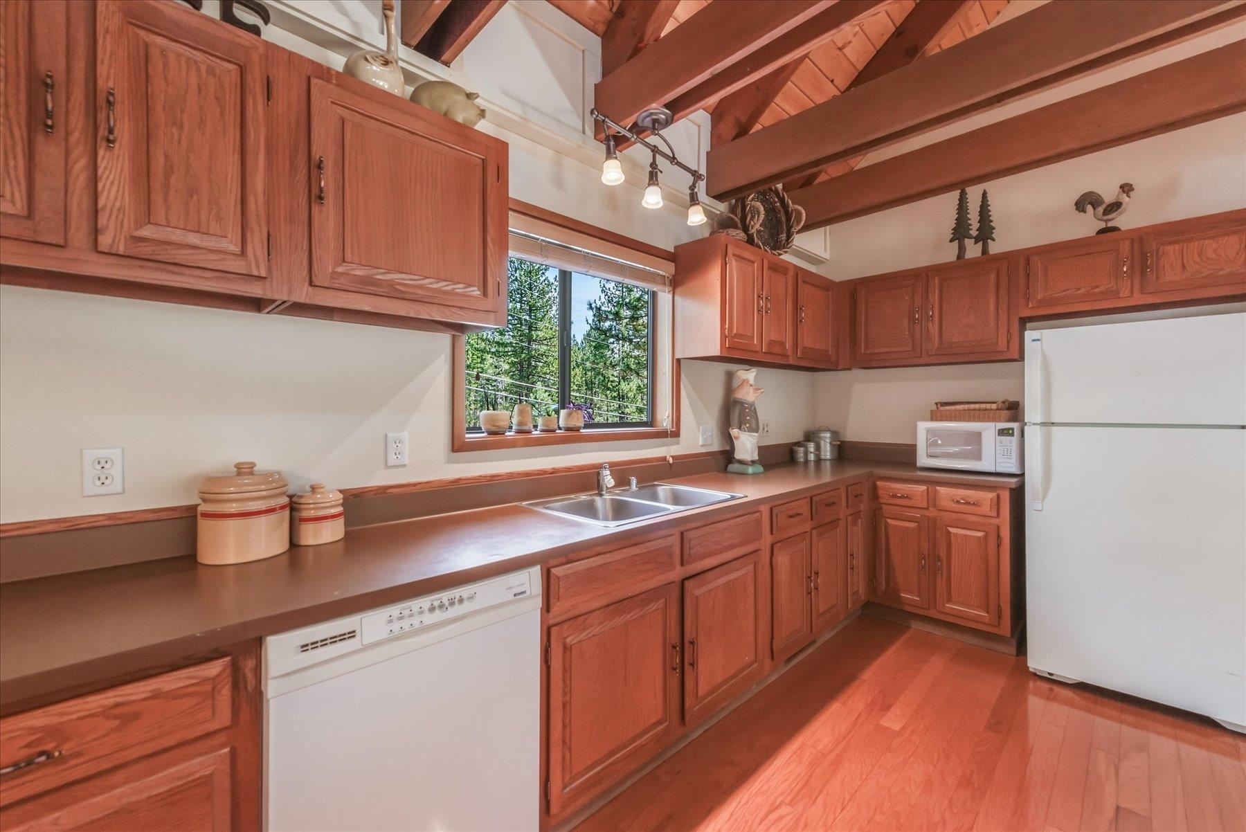 Kitchen with warm wood cabinets, exposed ceiling beams, and a window overlooking pine trees.