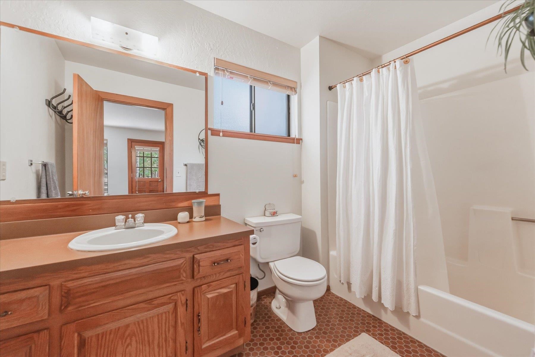 Bathroom with a wood vanity, large mirror, toilet, and tub behind a white shower curtain.