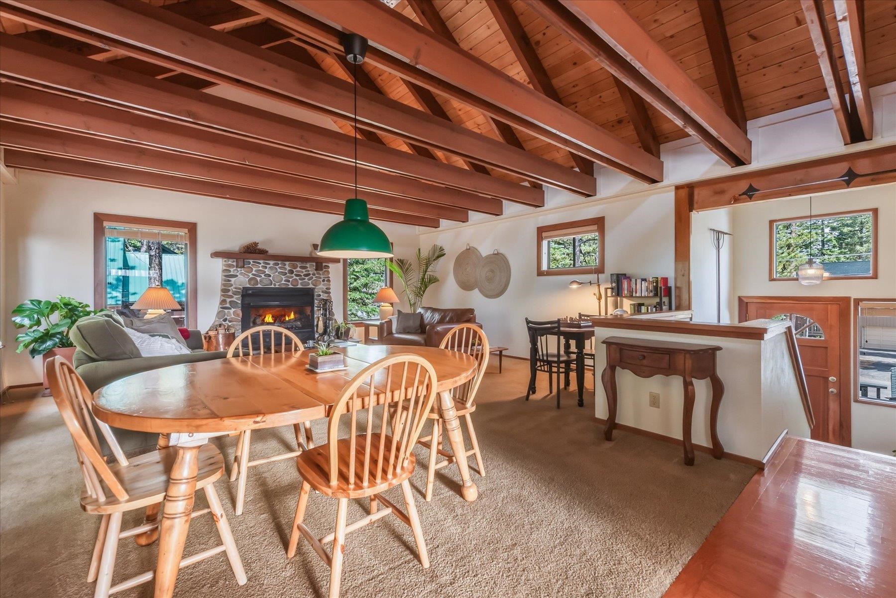 Open living and dining room with exposed wood beams, a stone fireplace, and a dining table.
