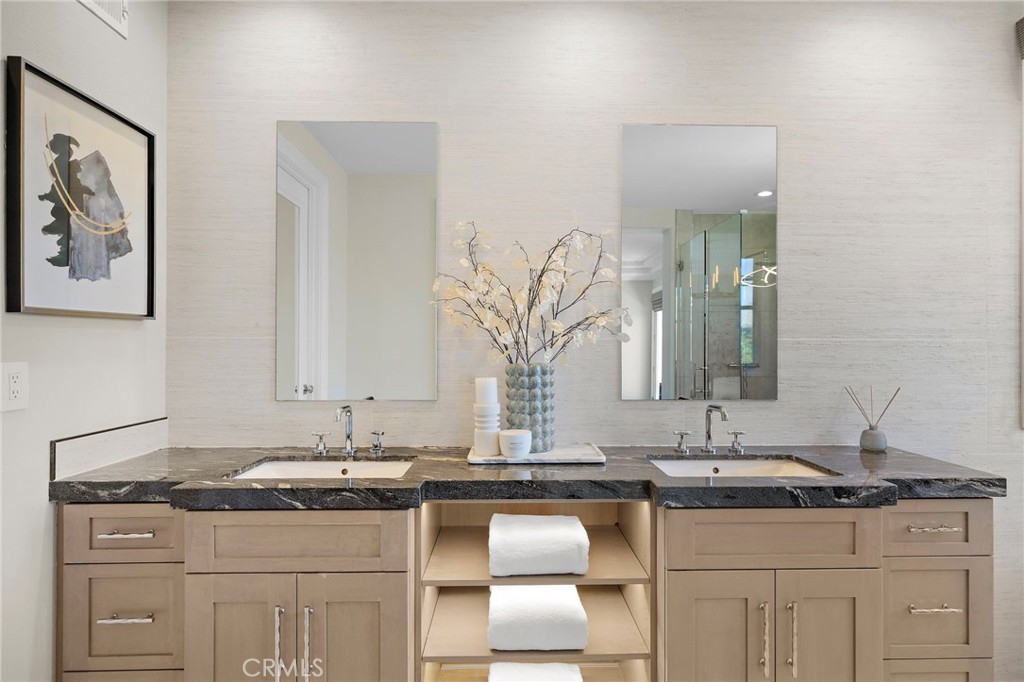 Bathroom double vanity with dark stone countertop, light wood cabinetry, and two mirrors.