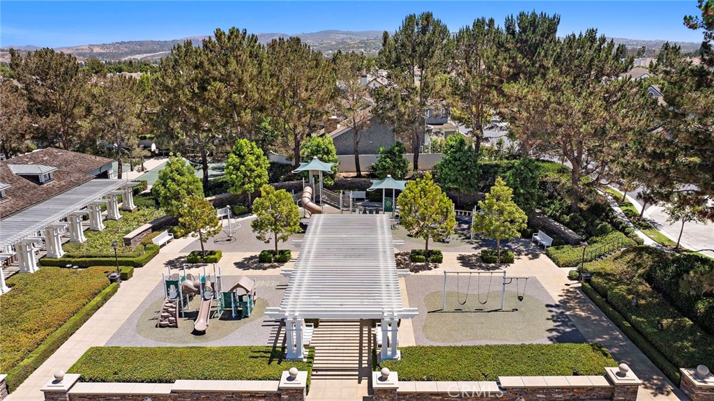 Community playground with slides and swings beneath a large pergola, surrounded by trees.