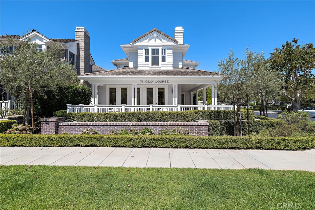 White two-story house with a columned front porch, framed by hedges and a broad green lawn.