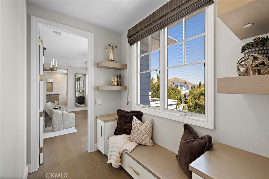 Built-in window seat with pillows beside a large window overlooking neighboring homes and trees.