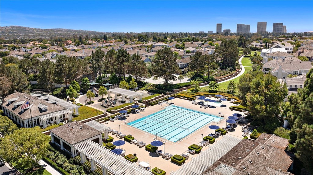 Aerial view of a community pool surrounded by homes, landscaped paths, and distant office towers.