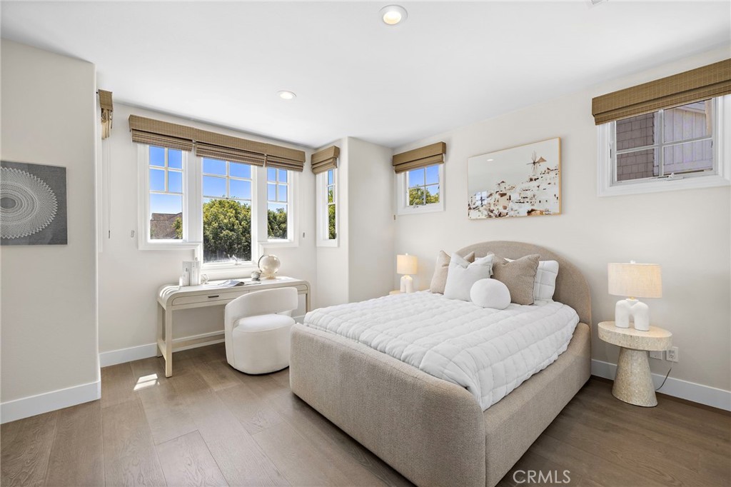 Staged bedroom with an upholstered bed, writing desk, and tall windows with woven shades.