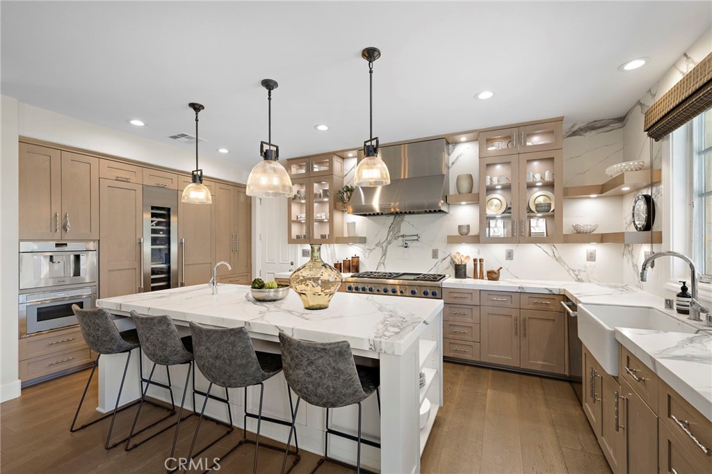 Kitchen with a marble island, warm wood cabinetry, stainless appliances, and pendant lights.
