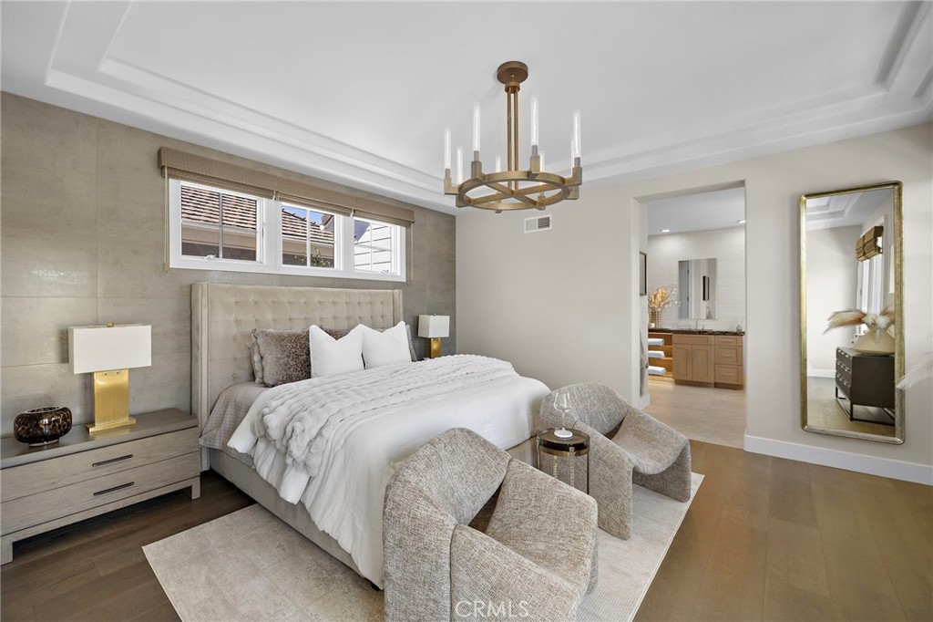 Primary bedroom with a white bed, upholstered headboard, two chairs, and a brass chandelier.