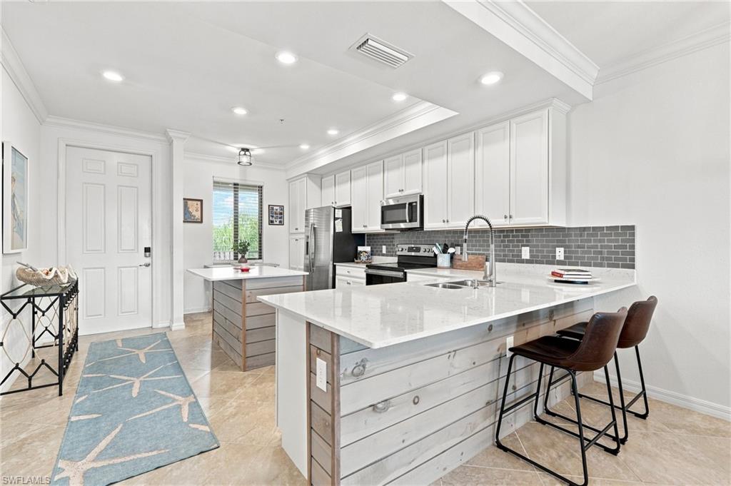 Bright kitchen with a large white island, gray tile backsplash, and stainless steel appliances.