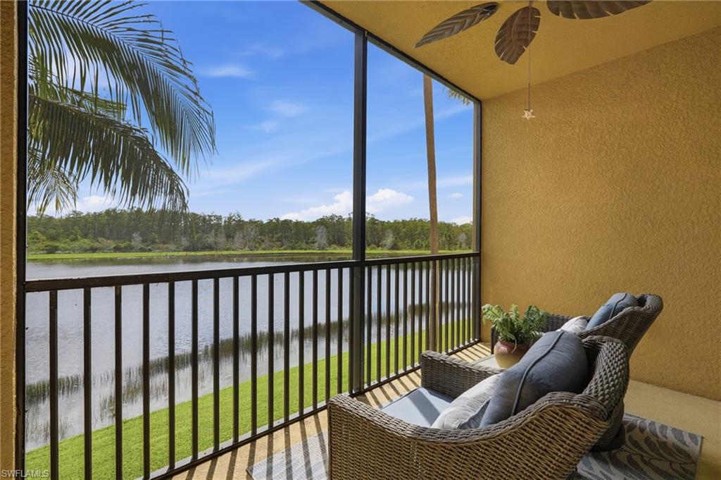Covered balcony with wicker seating overlooking a lake and grassy shoreline.