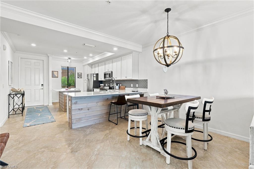 Kitchen and dining area with a large island, white cabinetry, and a dark wood table beneath a brass chandelier.