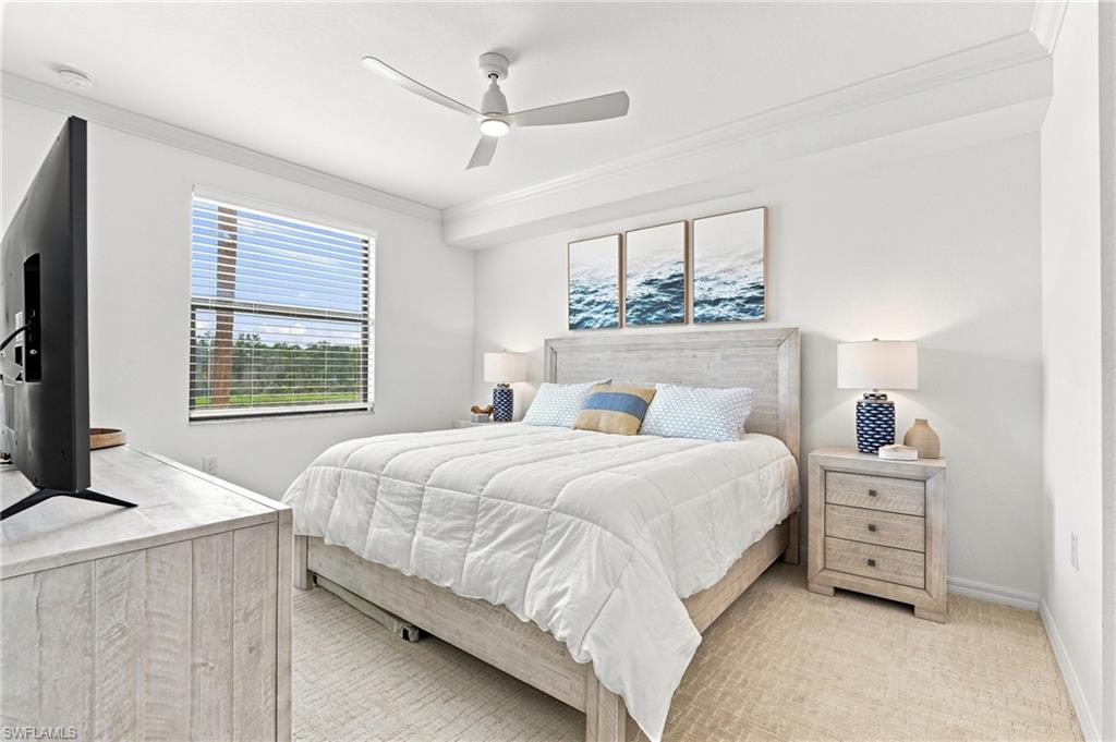 Staged bedroom with a white bed, light wood furniture, ceiling fan, and ocean prints above the headboard.