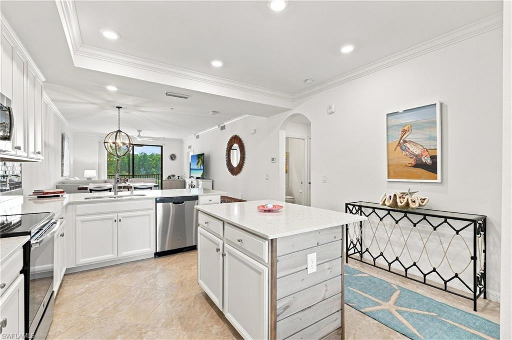 Bright white kitchen with a large island, stainless steel appliances, and sliding doors opening to greenery.