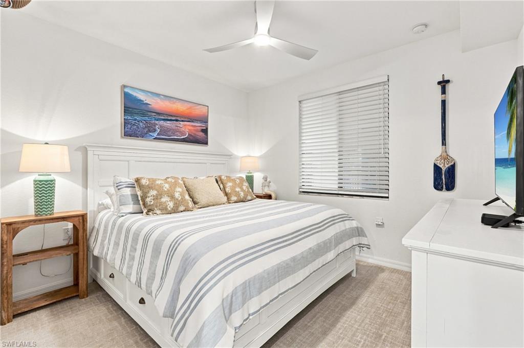 Furnished bedroom with a white bed, gray striped bedding, beach sunset artwork, and television.