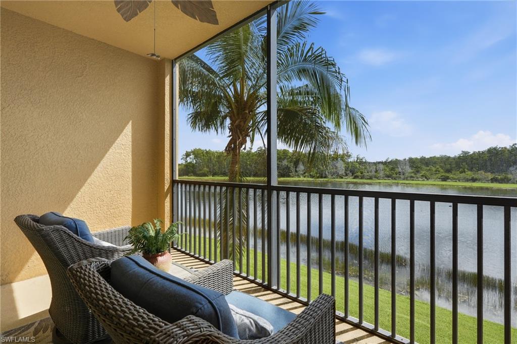 Furnished balcony overlooking a lake, with wicker seating and palm trees.