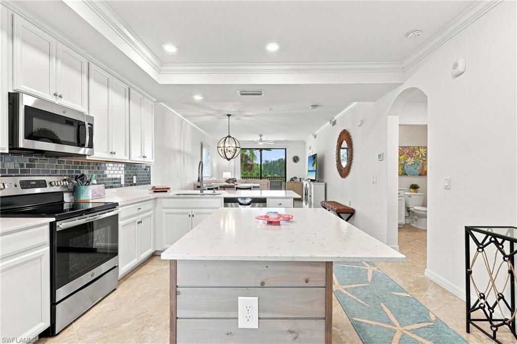 Open-plan kitchen with white cabinets, stainless steel appliances, and a large stone island.