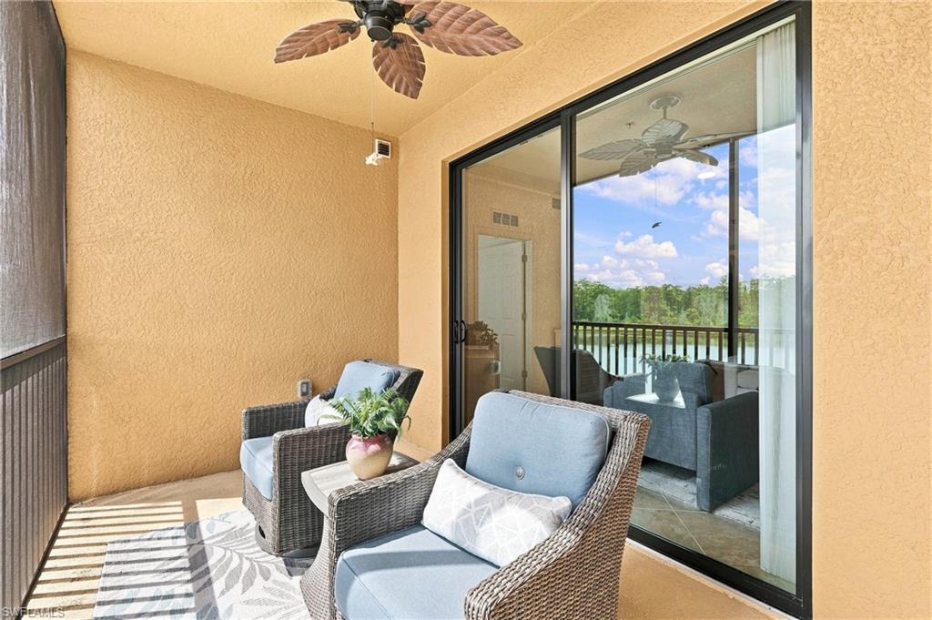 Covered lanai with wicker seating and a view of trees and water through sliding glass doors.