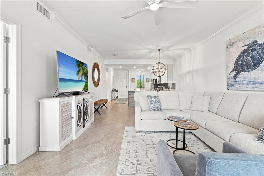 Furnished living room with a white sectional, coastal turtle artwork, and an open view into the kitchen.