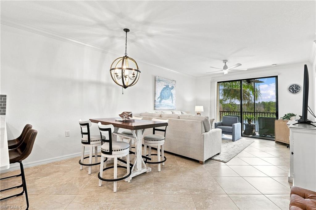 Open dining and living area with tiled floors, a globe chandelier, and sliding doors to a palm-lined lanai.