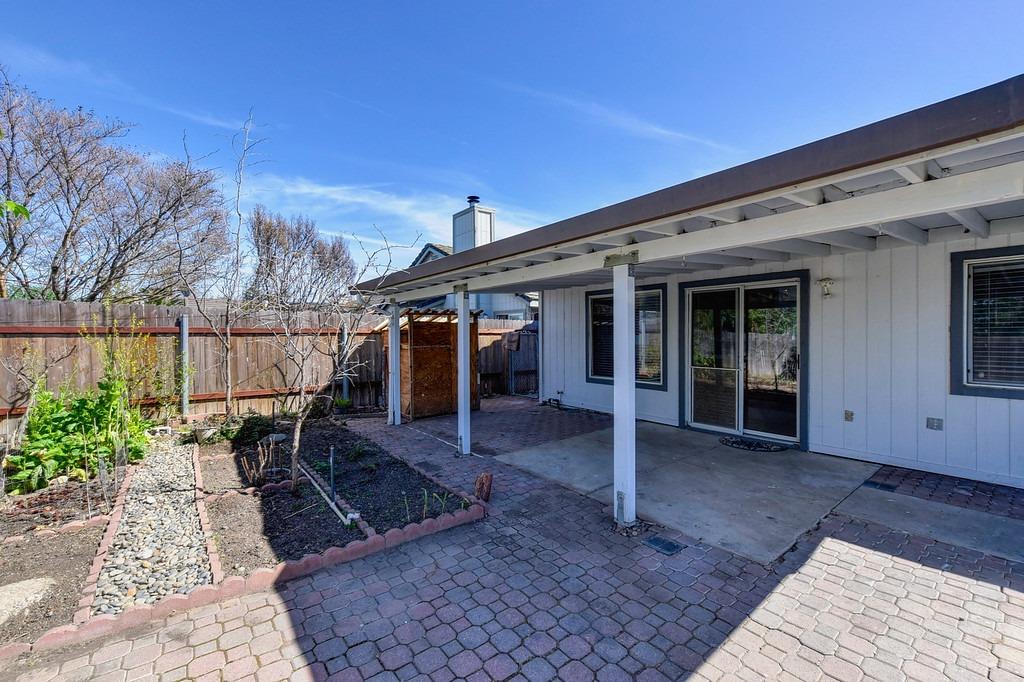 Covered backyard patio with paver courtyard, fenced garden beds, and a stone path.