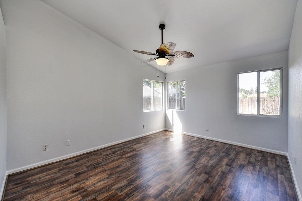 Empty room with dark wood-look flooring, multiple windows, and a ceiling fan with light.