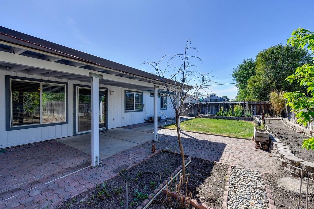 Backyard with a covered patio, brick pavers, lawn, and garden beds.