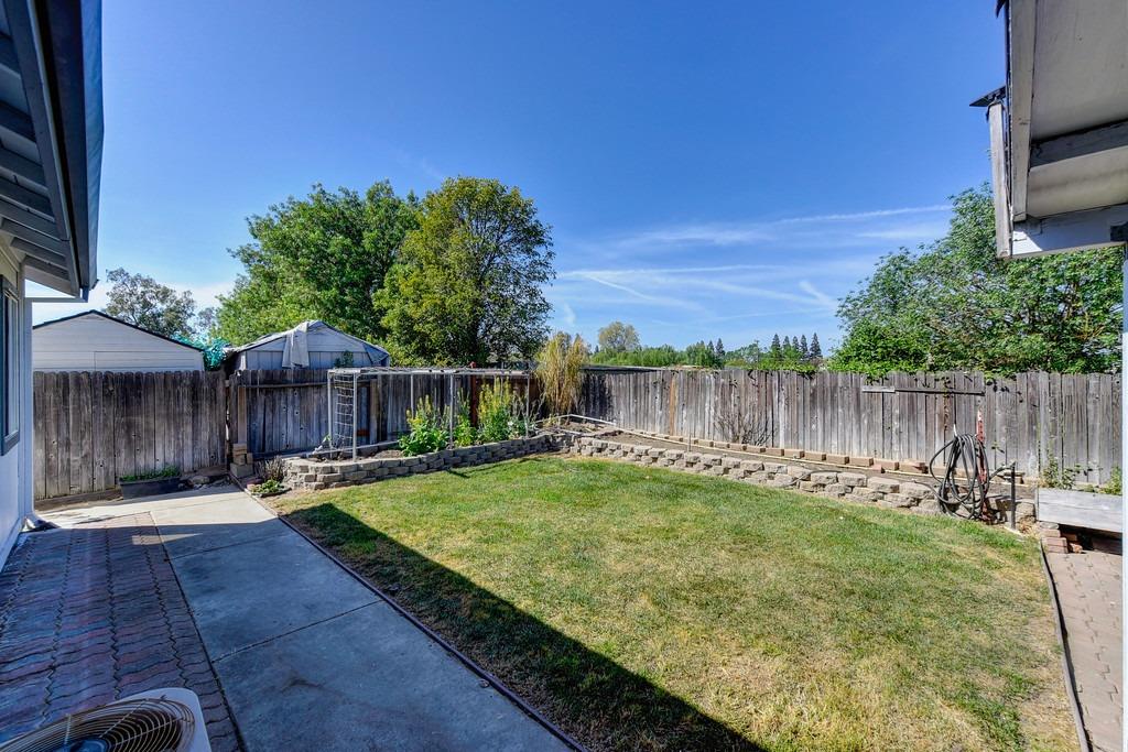 Fenced backyard with a lawn, raised stone garden beds, and paved patio.