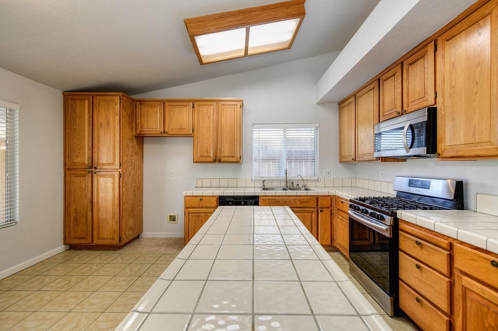 Kitchen with honey-colored wood cabinets, a large tiled island, and a gas range.