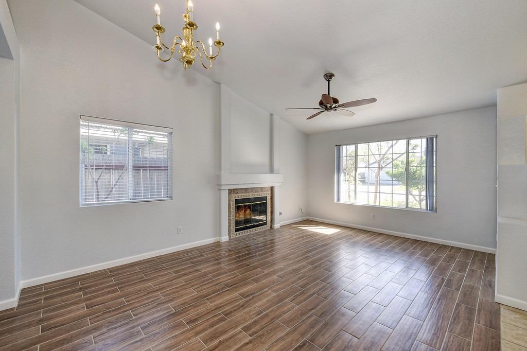 Vacant living room with a fireplace, brown tile flooring, and large windows.