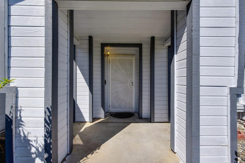 Covered home entrance with white siding, dark trim, and a sunburst-patterned front door.