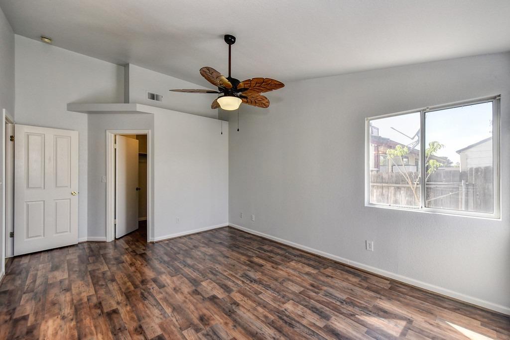 Empty bedroom with dark wood-look floors, a leaf-blade ceiling fan, and a large window overlooking a fenced yard.