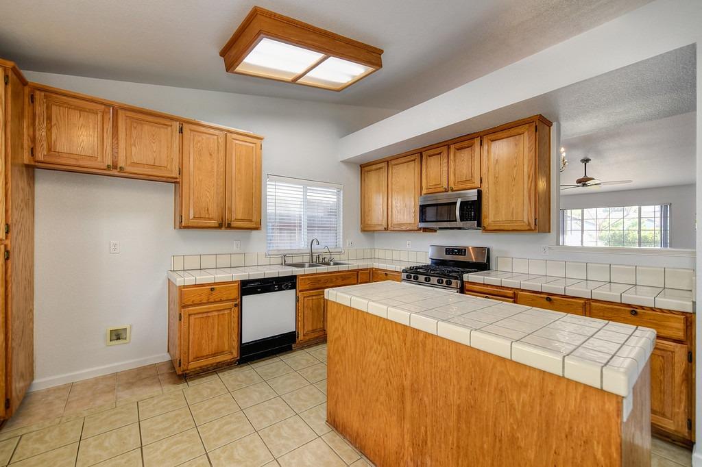 Kitchen with honey-colored cabinets, tiled counters, a large peninsula, and a gas range.