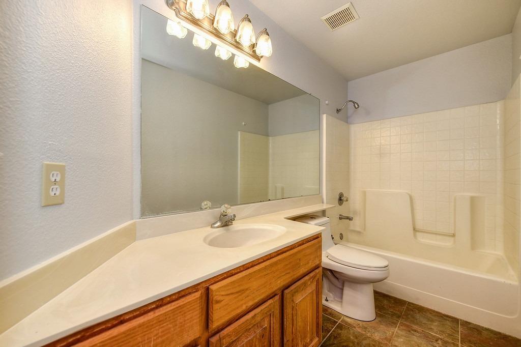 Bathroom with a wood vanity, large mirror, and white tub with molded grab handles.