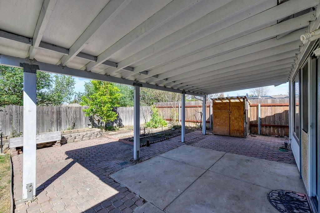 Covered backyard patio with brick pavers, a fenced planting bed, and a wooden shed.