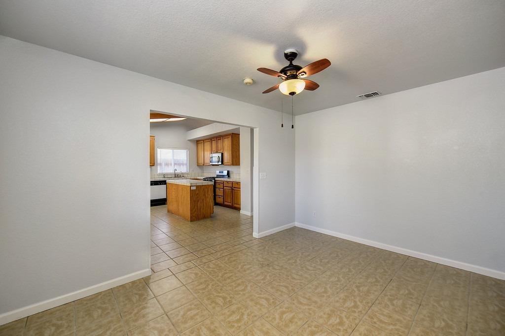 Empty dining area with tiled floors and a ceiling fan, opening to a wood-cabinet kitchen.