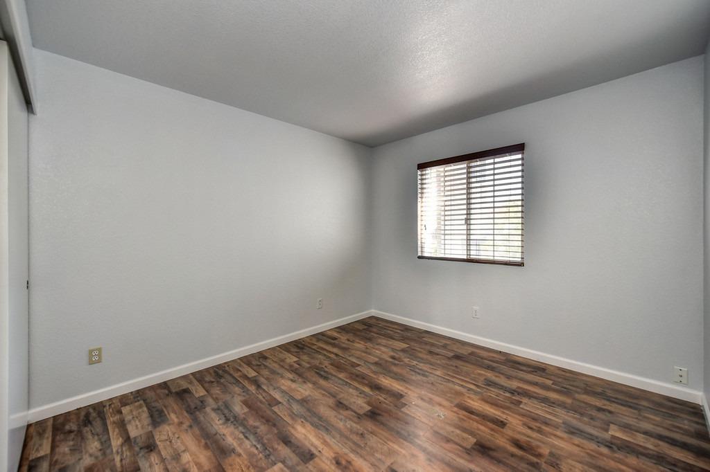 Empty room with wood-look flooring and a window with dark horizontal blinds.