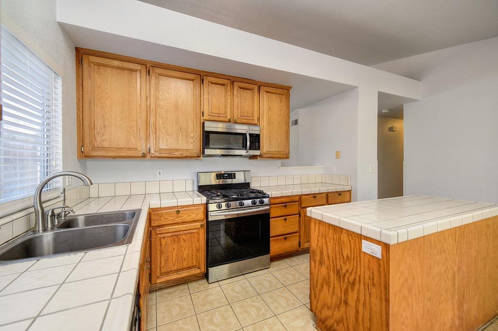 Kitchen with wood cabinets, tiled island, stainless steel range, and double-basin sink.