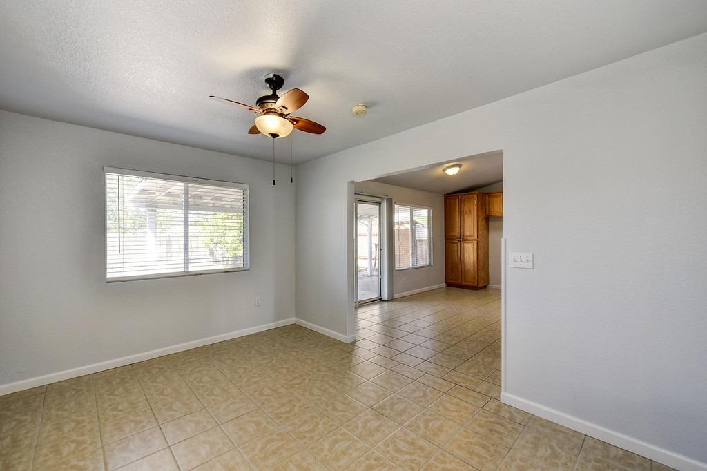 Empty tiled dining area with a ceiling fan and window, opening into a kitchen.