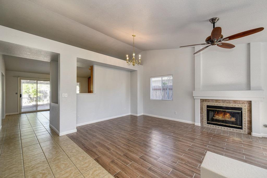 Empty living room with a tiled fireplace, wood-look flooring, and a ceiling fan.