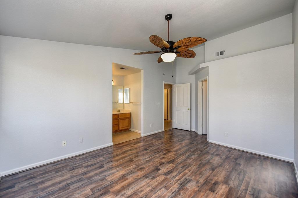 Empty bedroom with wood-look flooring, a leaf-blade ceiling fan, and an open doorway to the bathroom.