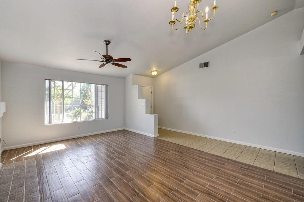 Vacant living and dining area with wood-look tile floors, a large window, ceiling fan, and chandelier.