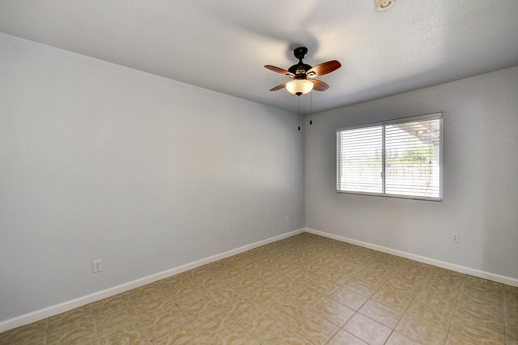 Empty room with tan tile flooring, a window with blinds, and a ceiling fan with a light.